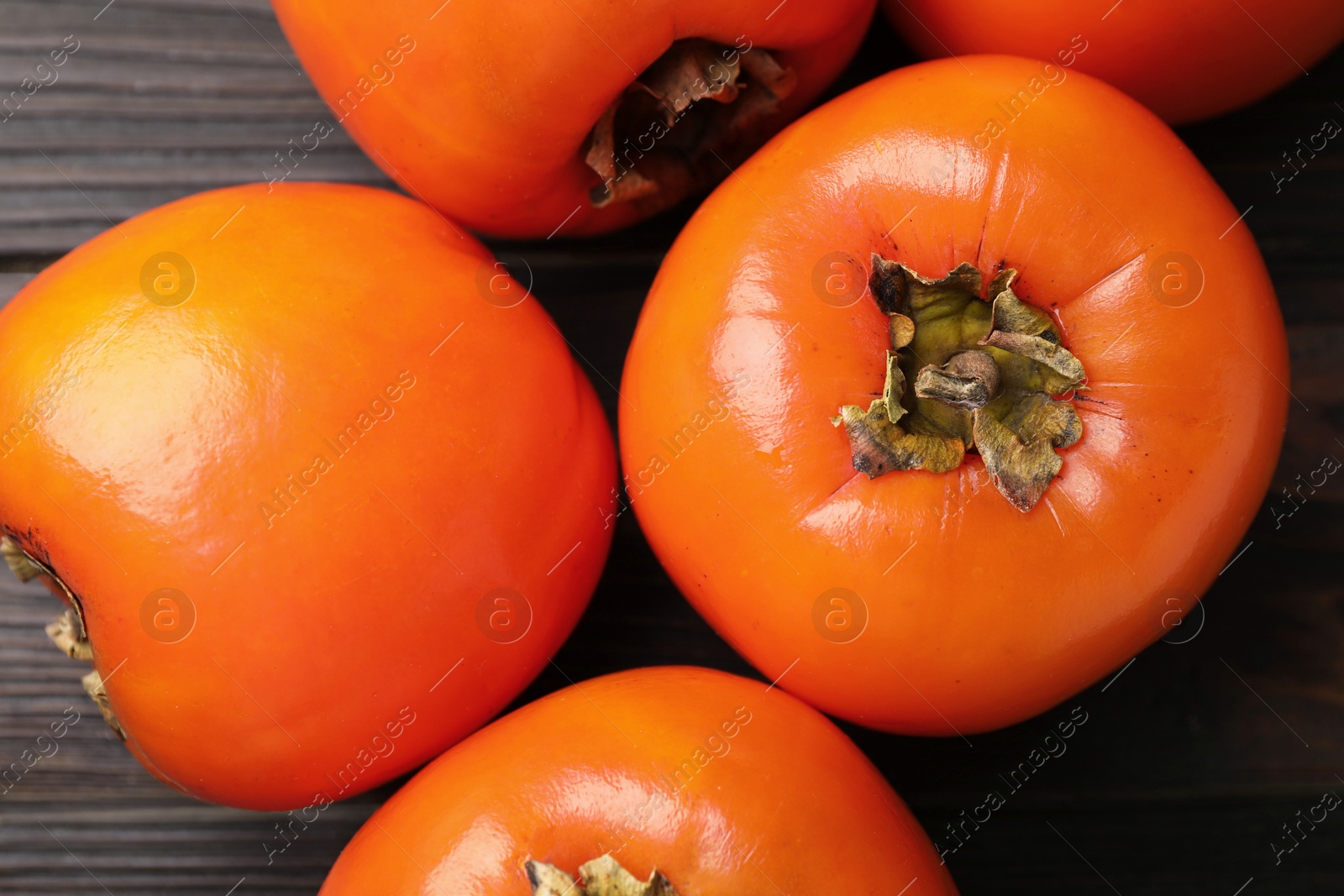 Photo of Delicious ripe persimmons on dark wooden table, top view