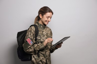 Photo of Female cadet with backpack and tablet on light grey background. Military education
