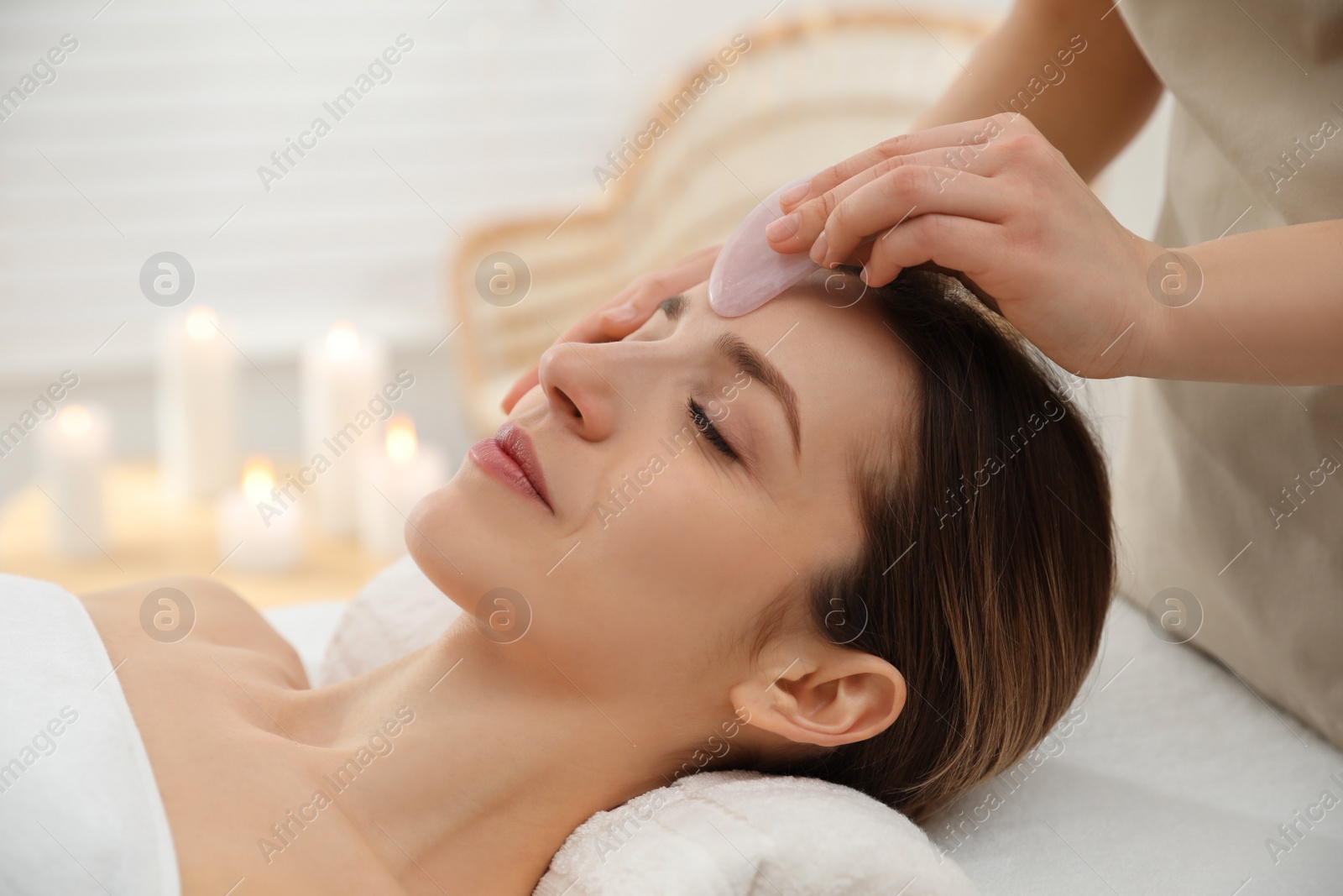 Photo of Young woman receiving facial massage with gua sha tool in beauty salon