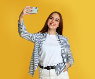 Photo of Young woman taking selfie on yellow background