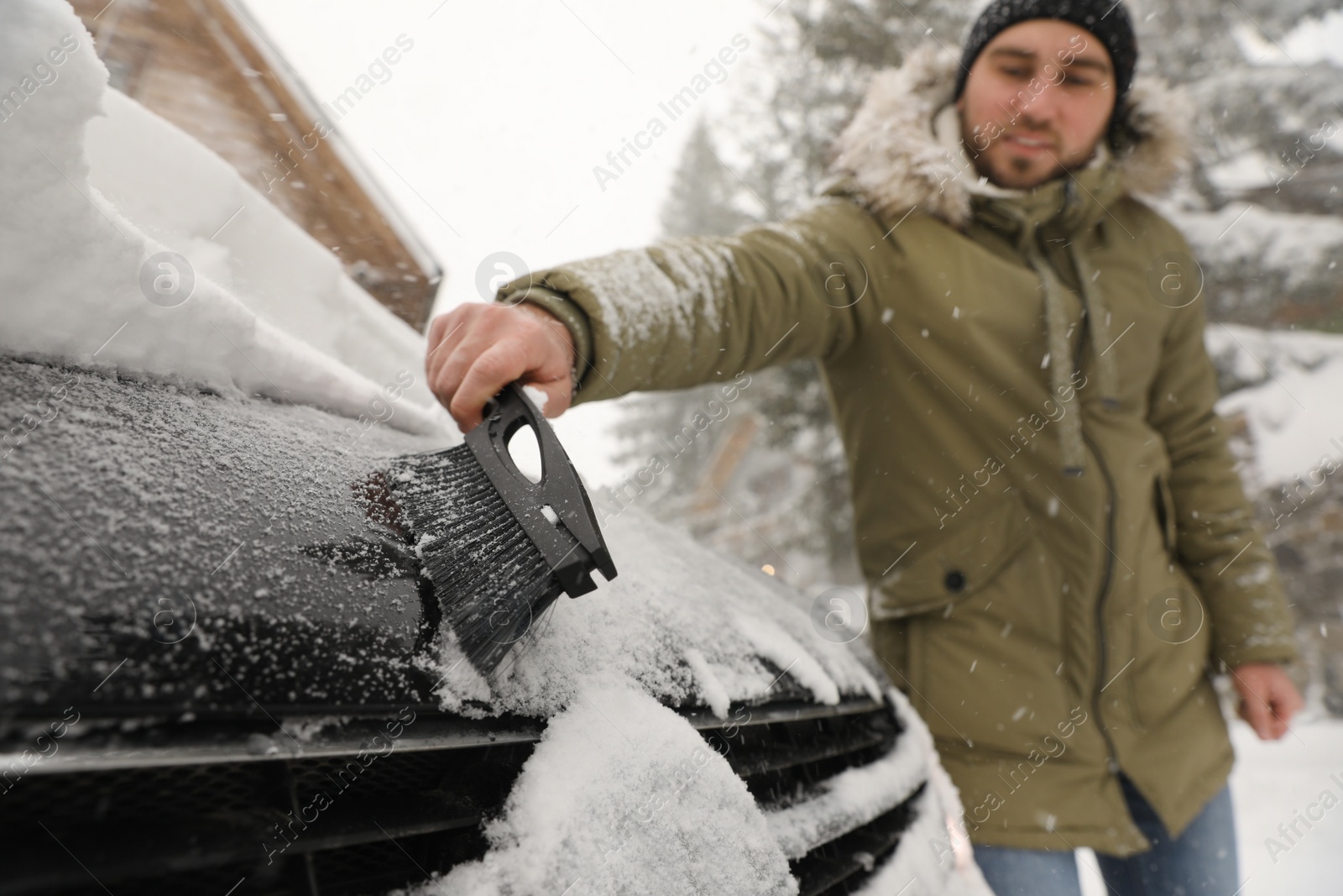 Photo of Young man cleaning snow from car outdoors on winter day