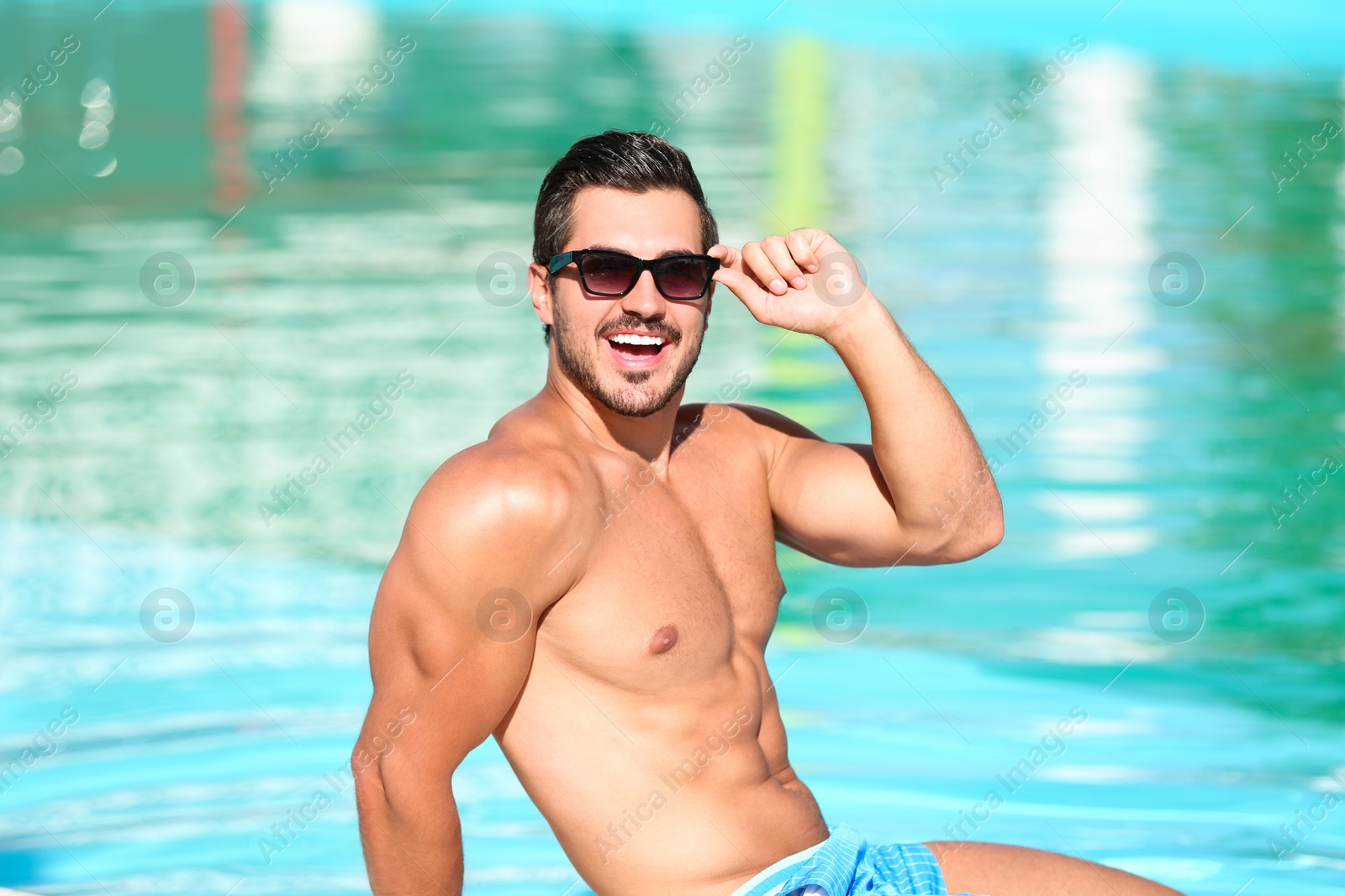 Photo of Handsome young man with sunglasses near swimming pool on sunny day