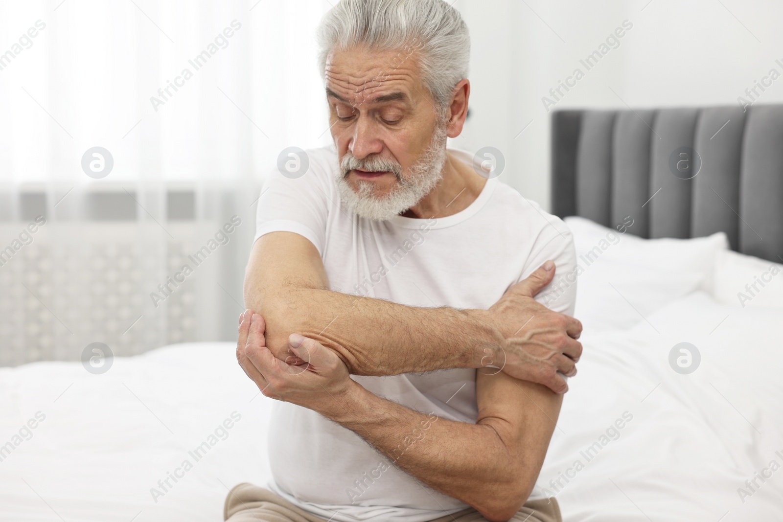 Photo of Arthritis symptoms. Man suffering from pain in elbow on bed at home