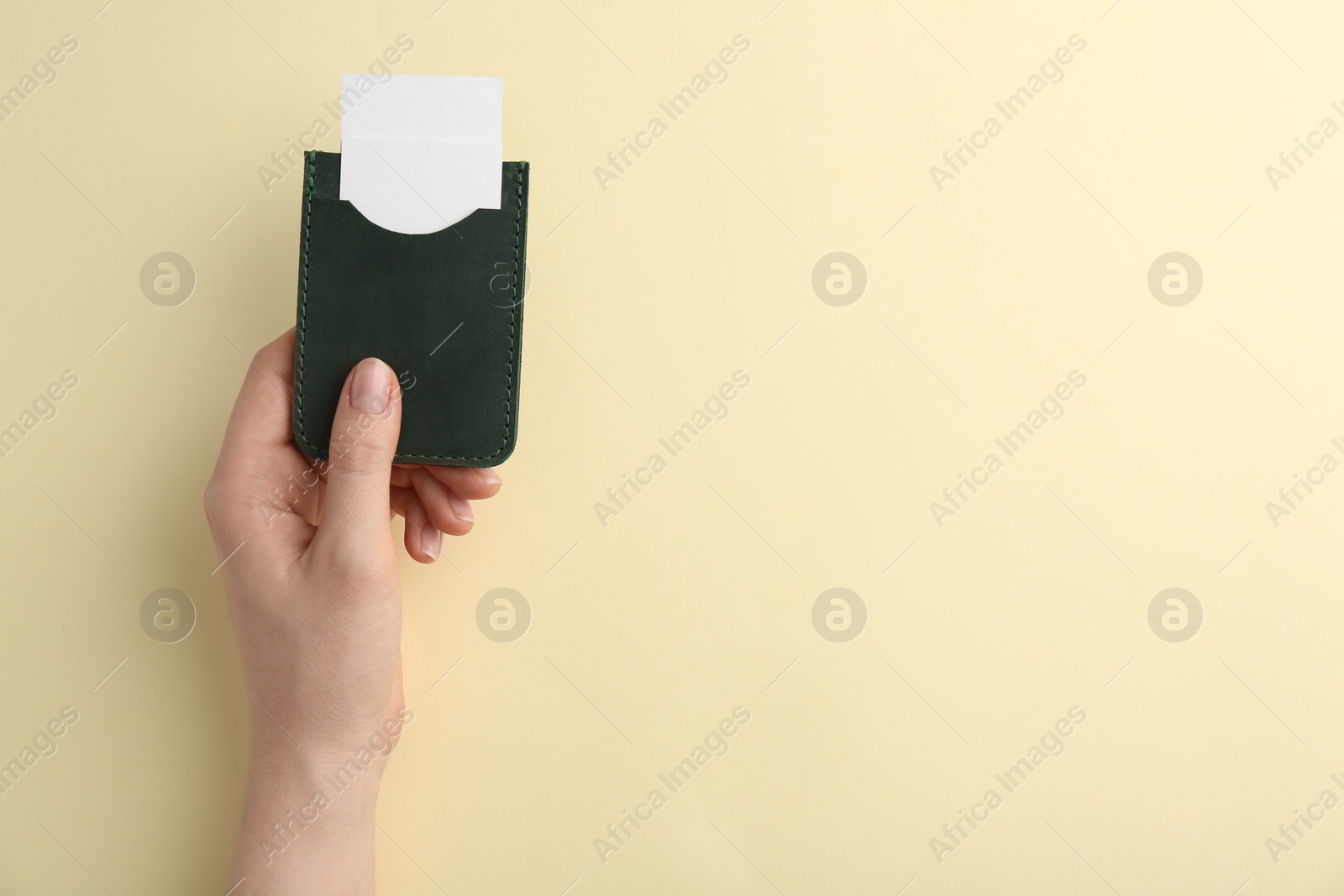 Photo of Woman holding business card holder with blank cards on light yellow background, top view. Space for text