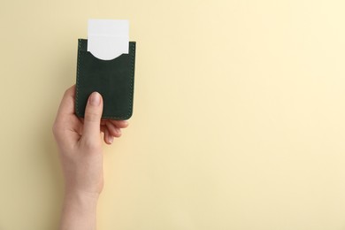 Photo of Woman holding business card holder with blank cards on light yellow background, top view. Space for text