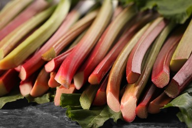 Many ripe rhubarb stalks and leaves on dark table, closeup