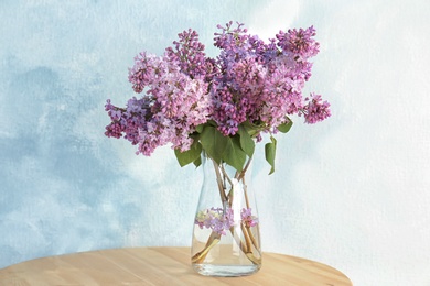 Photo of Vase with beautiful blossoming lilac on table against light background. Spring flowers