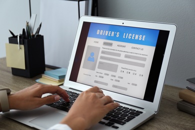 Photo of Woman using laptop to fill driver's license application form at table in office, closeup