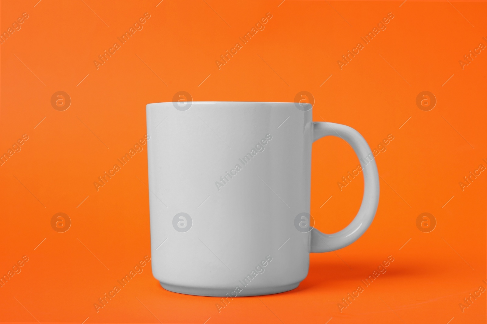 Photo of One white ceramic mug on orange background