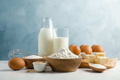 Fresh ingredients for delicious homemade cake on white wooden table against blue background