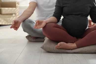 Photo of Young pregnant woman with her husband practicing yoga at home, closeup
