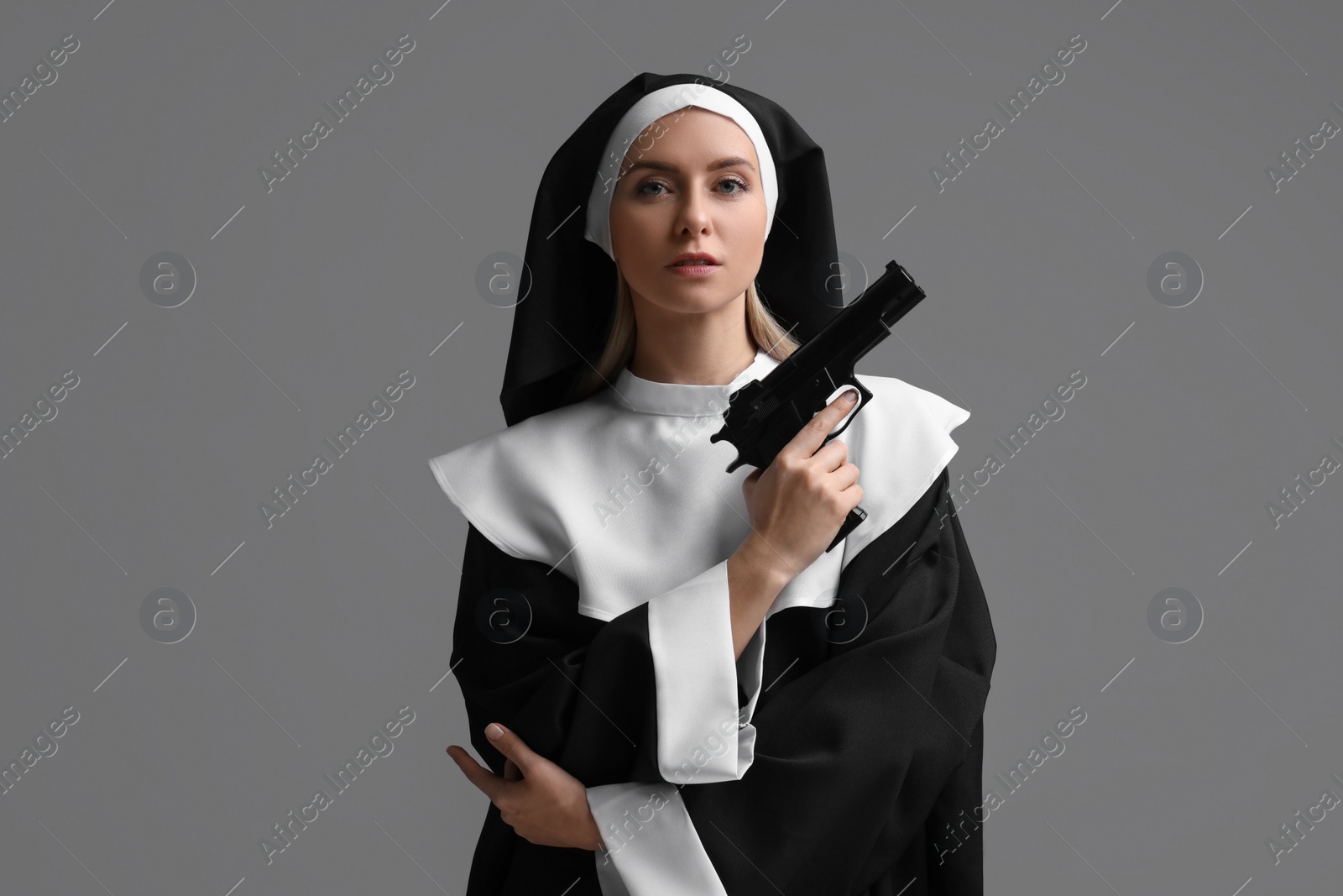 Photo of Woman in nun habit holding handgun on grey background