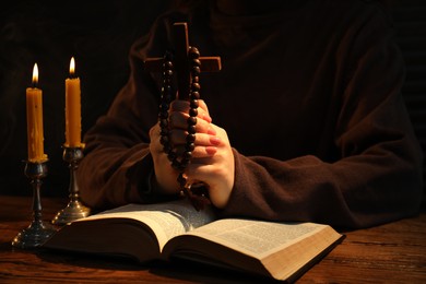 Woman praying at table with burning candles and Bible, closeup