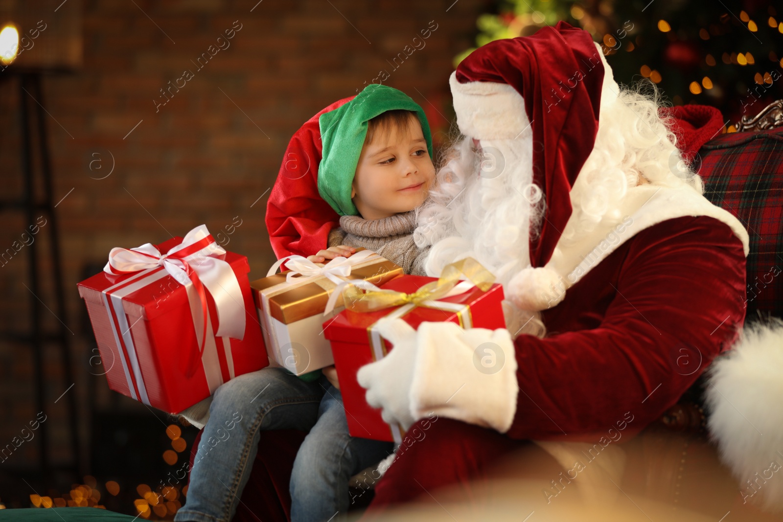 Photo of Santa Claus and little boy with Christmas gifts indoors