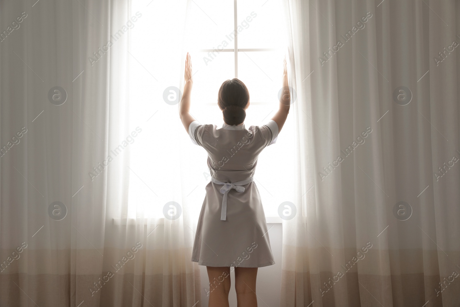 Photo of Young maid opening curtains in hotel room
