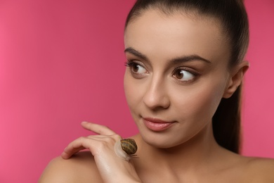 Photo of Beautiful young woman with snail on her hand against pink background