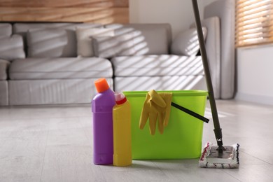 Photo of Floor mop, cleaning detergents and bucket with gloves in living room