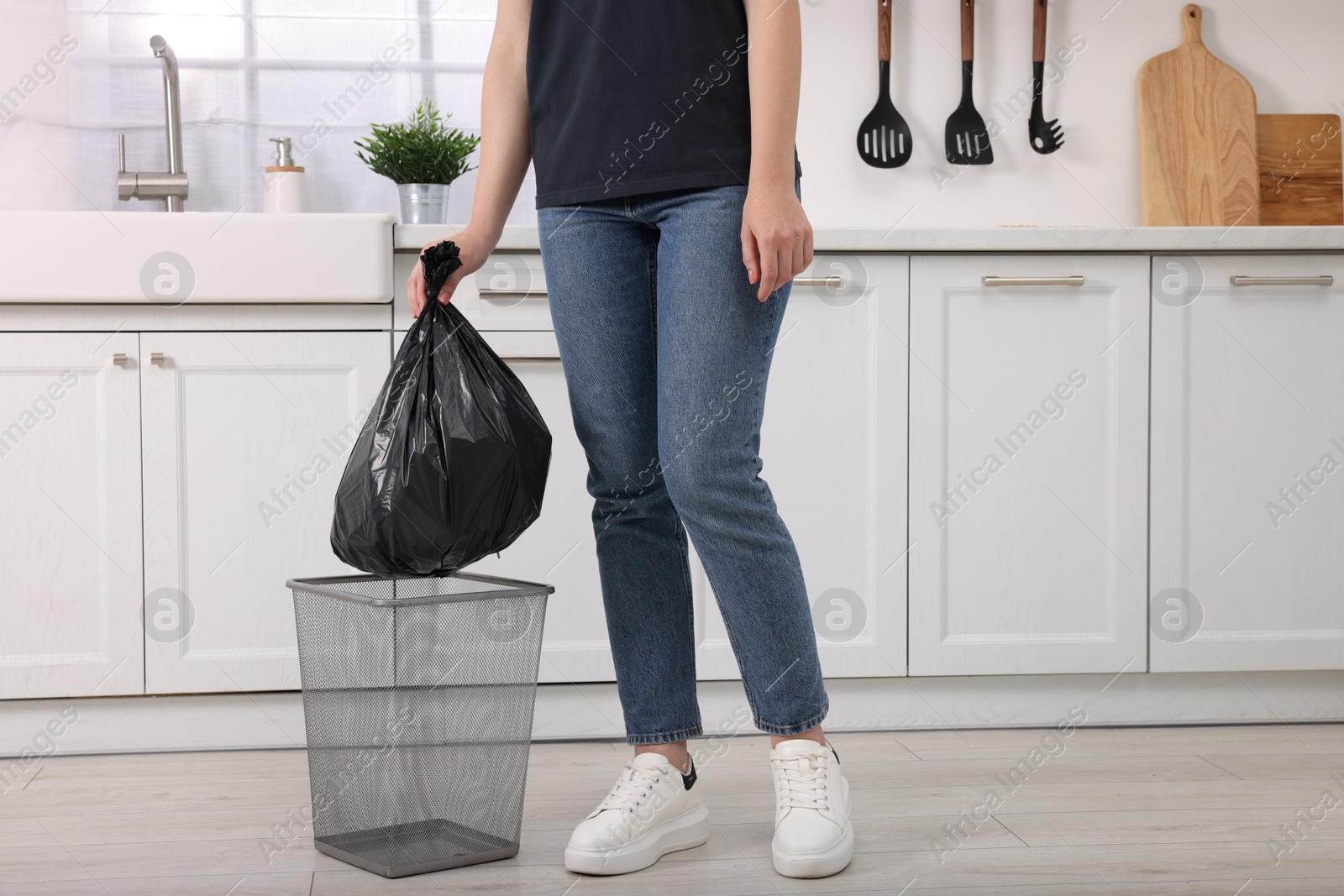 Photo of Woman taking garbage bag out of trash bin in kitchen, closeup