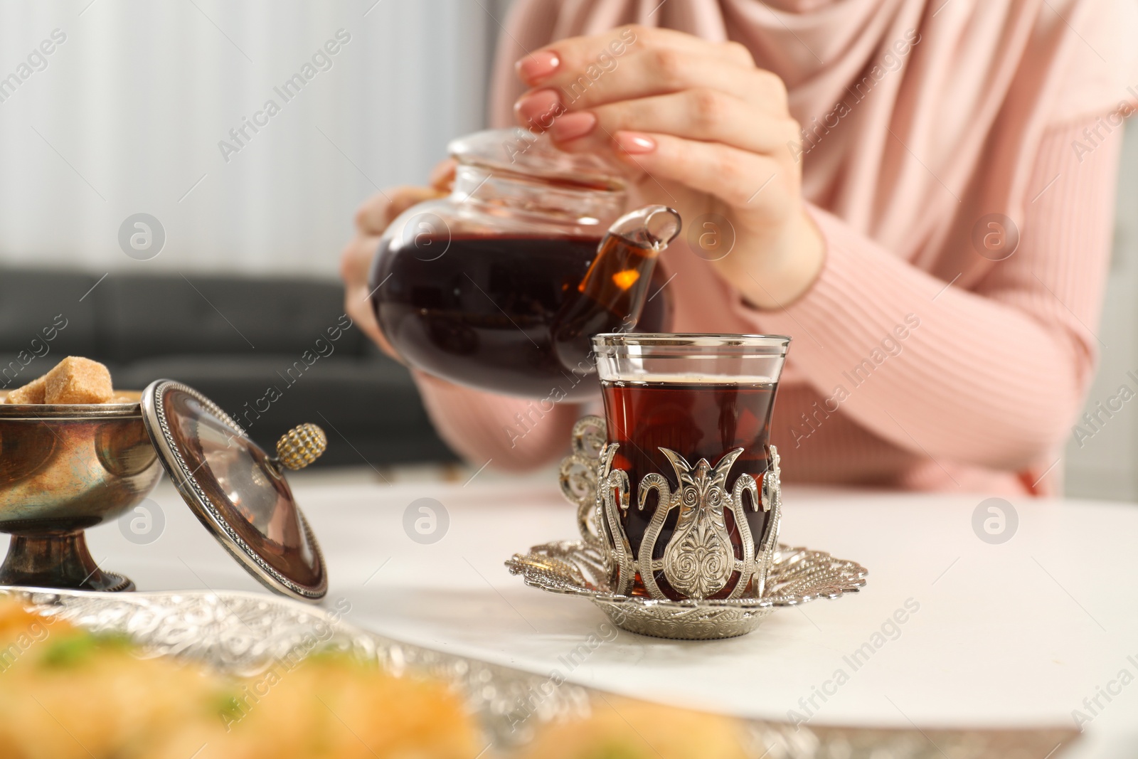 Photo of Woman pouring delicious Turkish tea from teapot into cup at white table, closeup