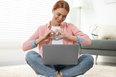 Woman making heart with hands during video chat via laptop at home. Long-distance relationship