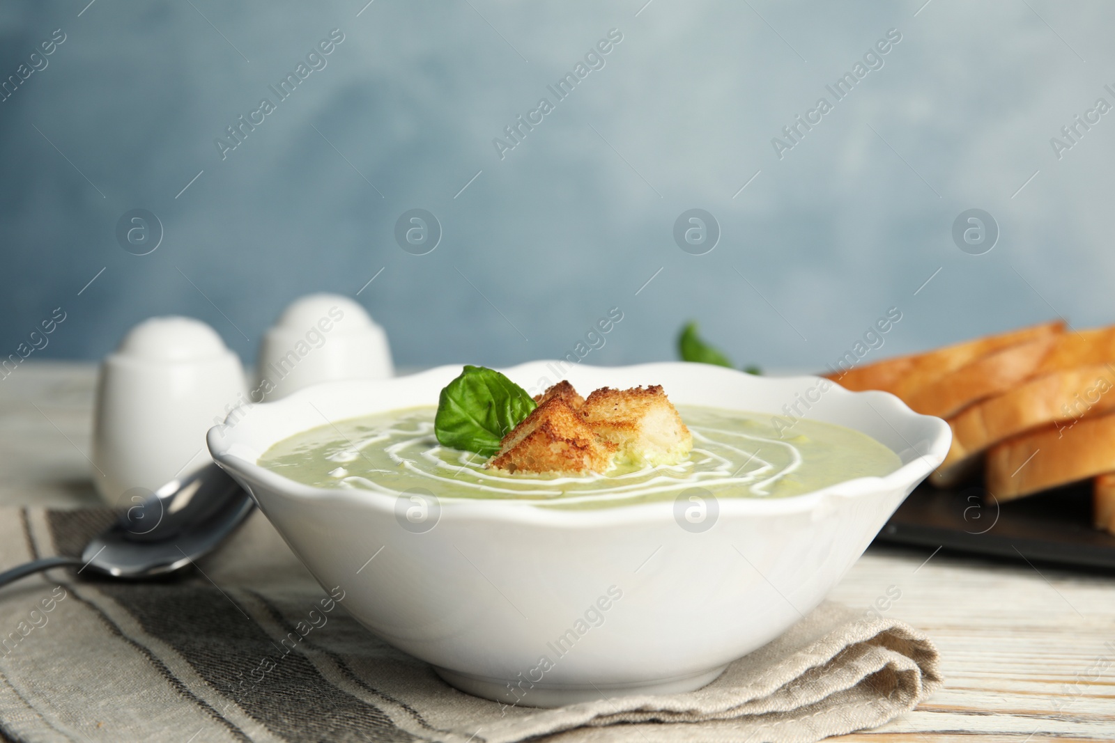 Photo of Delicious broccoli cream soup with croutons served on white wooden table. Space for text