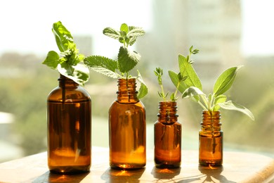 Bottles of essential with and fresh herbs on wooden table indoors