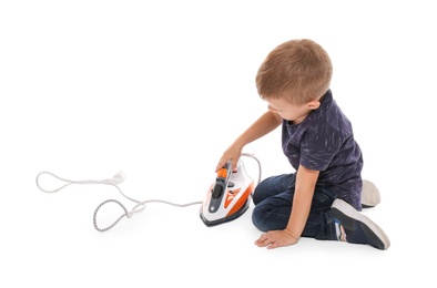 Little boy playing with iron on white background. Danger at home