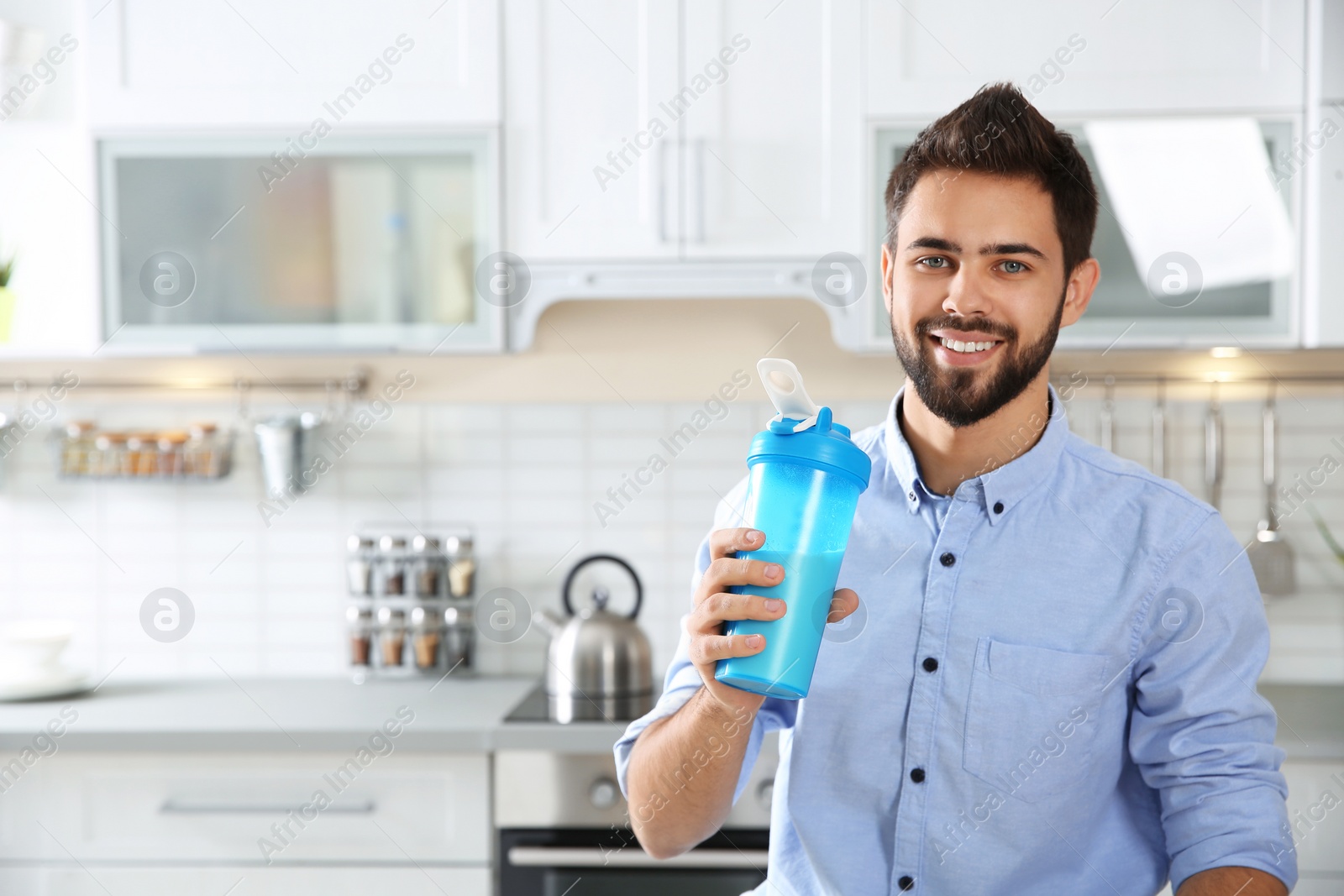 Photo of Young man holding bottle of protein shake in kitchen. Space for text