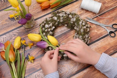 Photo of Woman decorating willow wreath with tulip flowers at wooden table, closeup