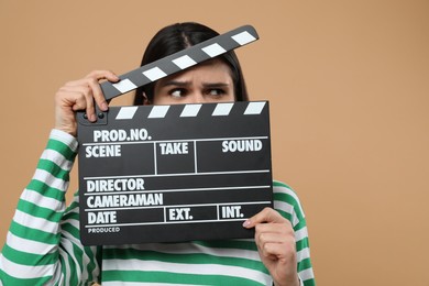 Emotional actress with clapperboard on beige background. Film industry