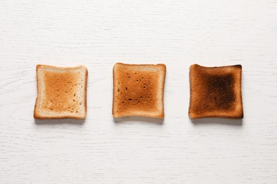 Slices of delicious toasted bread on white wooden table, top view