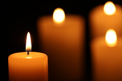 Photo of Burning candles on black background, closeup. Space for text