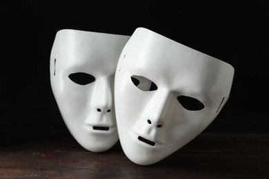 Photo of White theatre masks on wooden table against black background