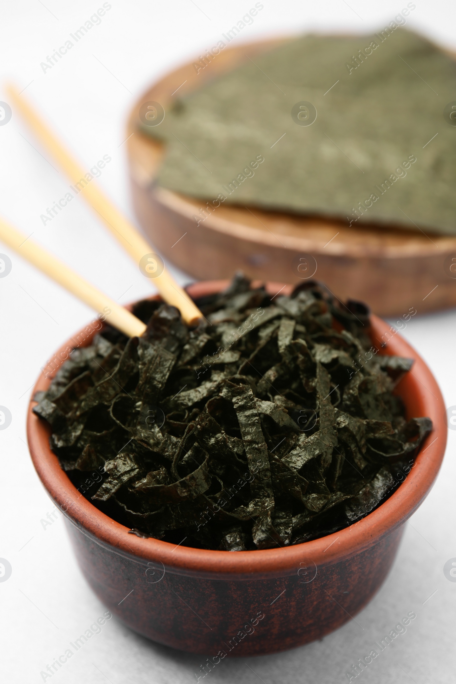 Photo of Bowl with chopped nori sheets and chopsticks on white table, closeup