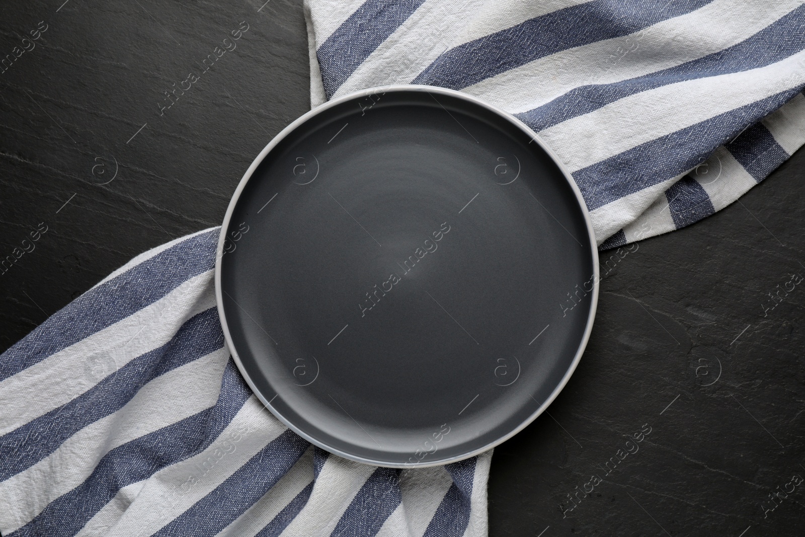Photo of New clean plate and napkin on black table, top view