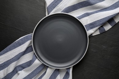 Photo of New clean plate and napkin on black table, top view