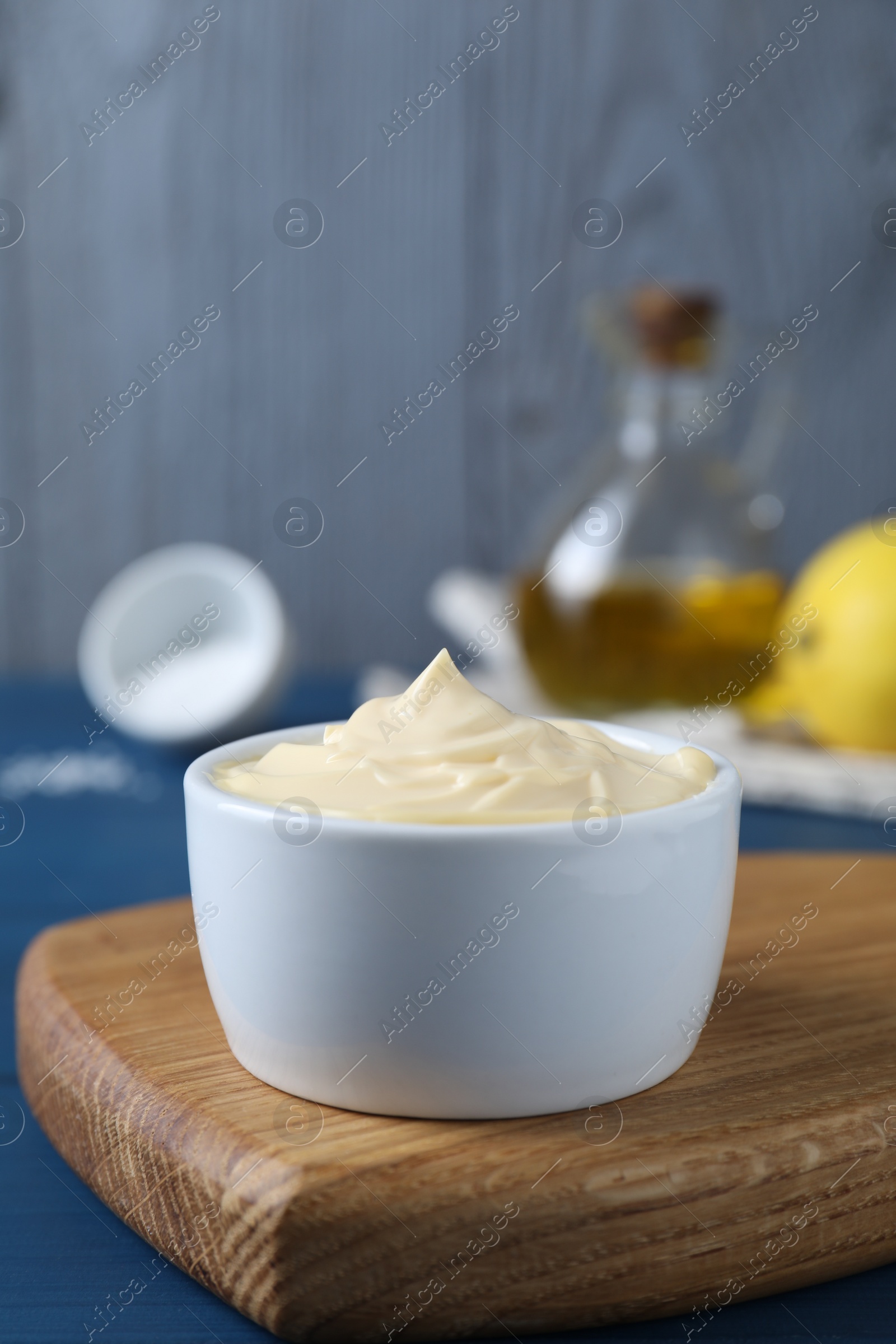 Photo of Tasty mayonnaise in bowl on blue table, closeup