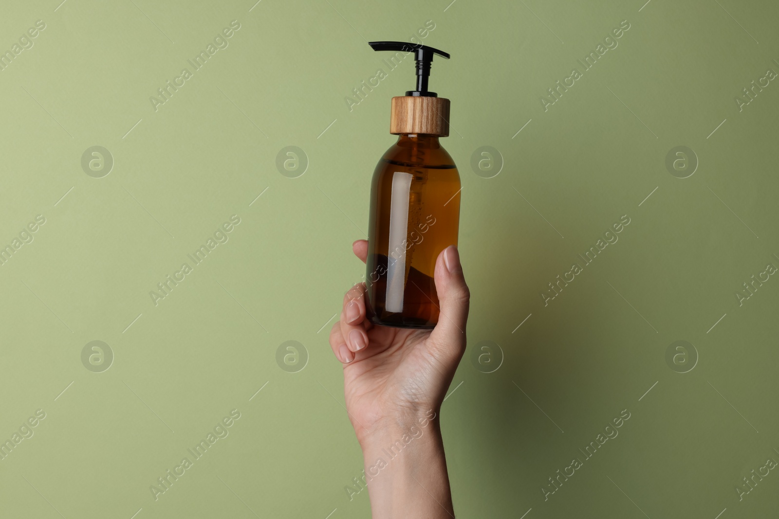 Photo of Woman holding bottle of cosmetic product on pale olive background, closeup. Space for text