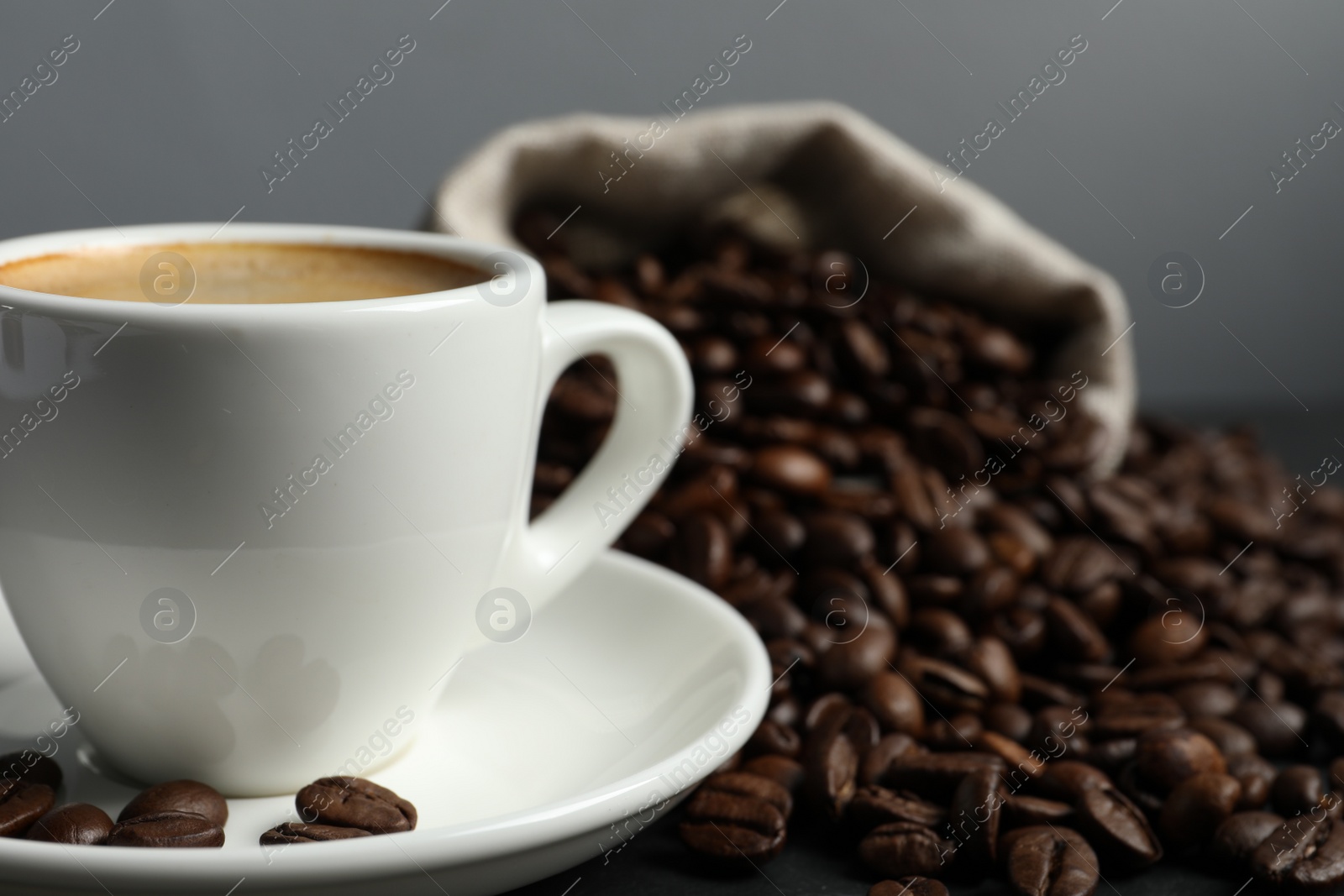 Photo of Cup of aromatic coffee and beans on grey table, closeup. Space for text