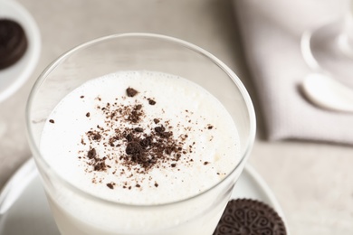 Glass of milk with chocolate cookie crumbs on table, closeup