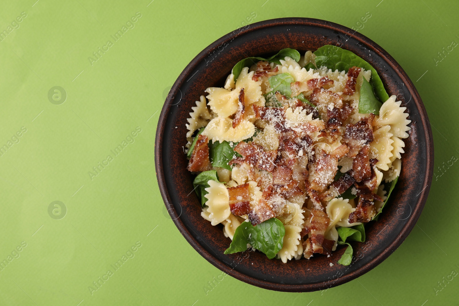 Photo of Tasty pasta with bacon and basil on light green table, top view. Space for text