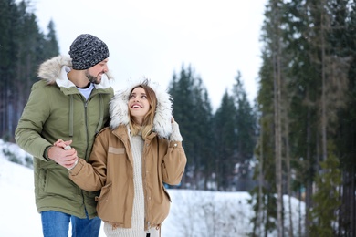 Happy couple near conifer forest on snowy day, space for text. Winter vacation