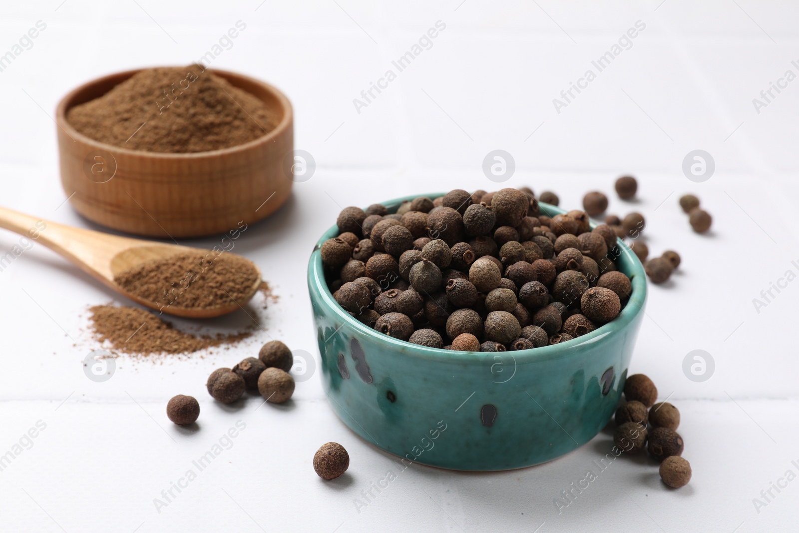 Photo of Ground and whole allspice berries (Jamaica pepper) on white tiled table, closeup