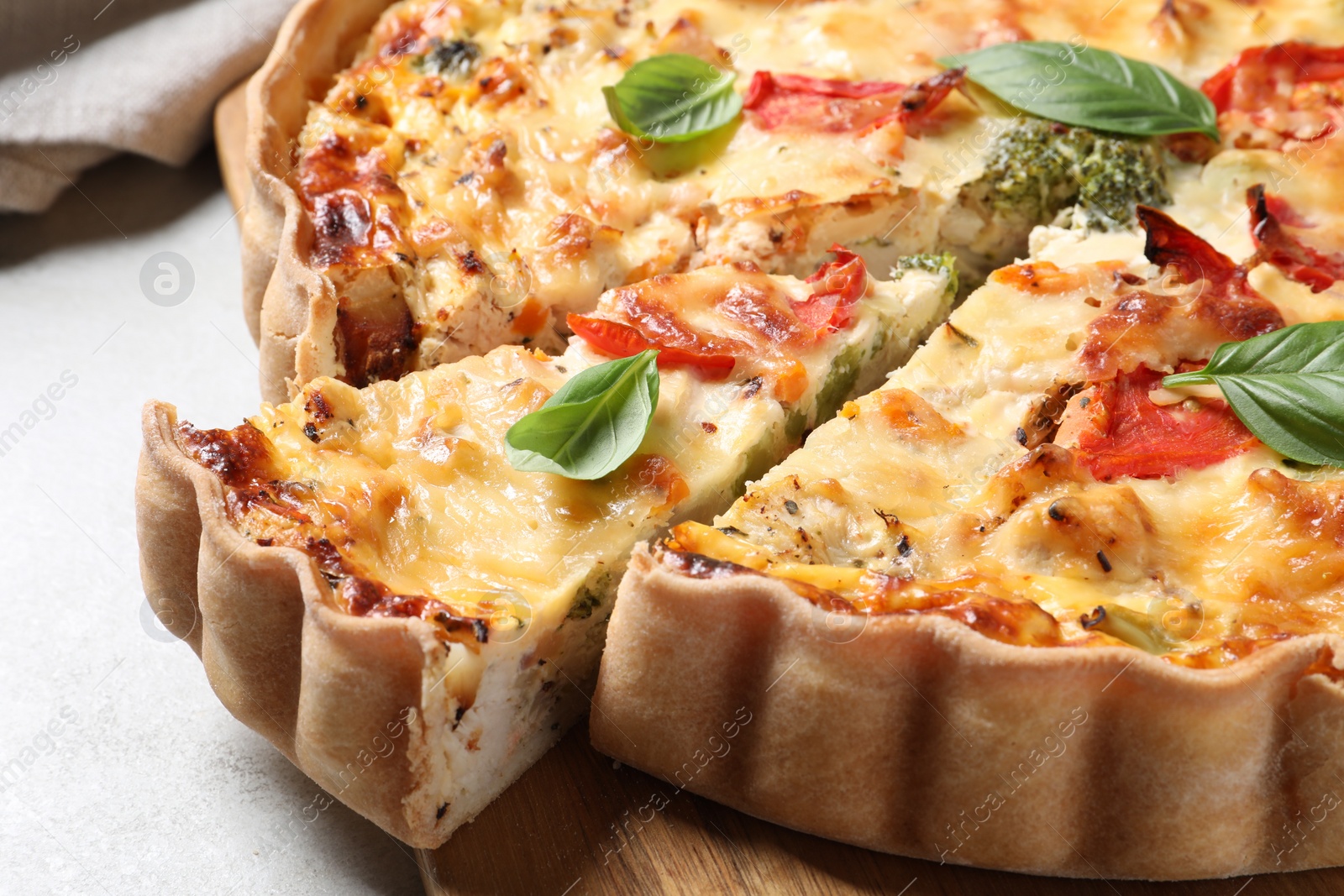Photo of Tasty quiche with tomatoes, basil and cheese on light textured table, closeup