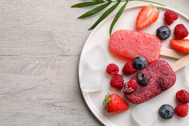 Plate of tasty fruit ice pops with berries on light wooden table, flat lay. Space for text