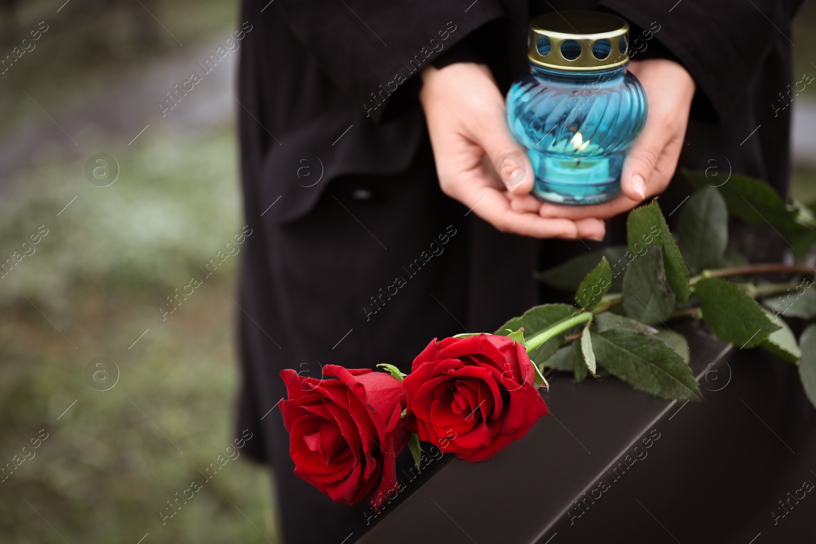 Photo of Woman with candle outdoors, focus on red roses. Funeral ceremony