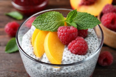 Photo of Delicious chia pudding with raspberries, peach and mint in glass, closeup
