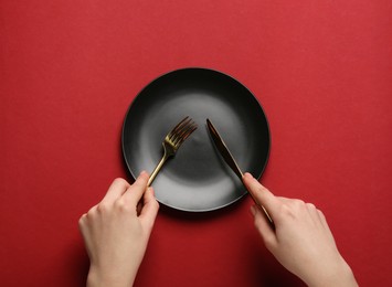 Photo of Woman with empty plate and cutlery on red background, top view