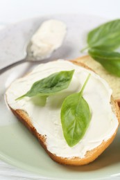 Photo of Pieces of bread with cream cheese and basil leaves on white wooden table, closeup
