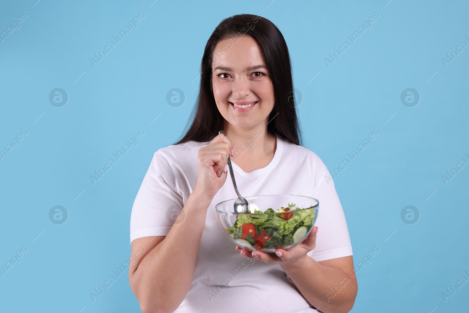 Photo of Beautiful overweight woman eating salad on light blue background. Healthy diet